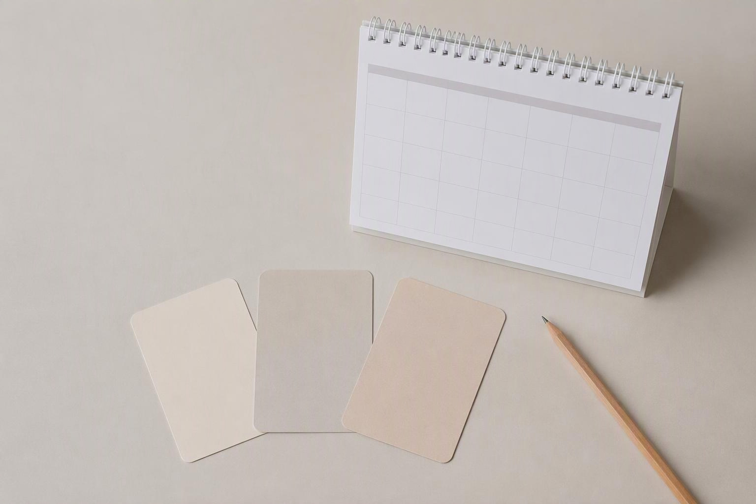 Cartões em branco, calendário e lápis organizados sobre uma mesa.