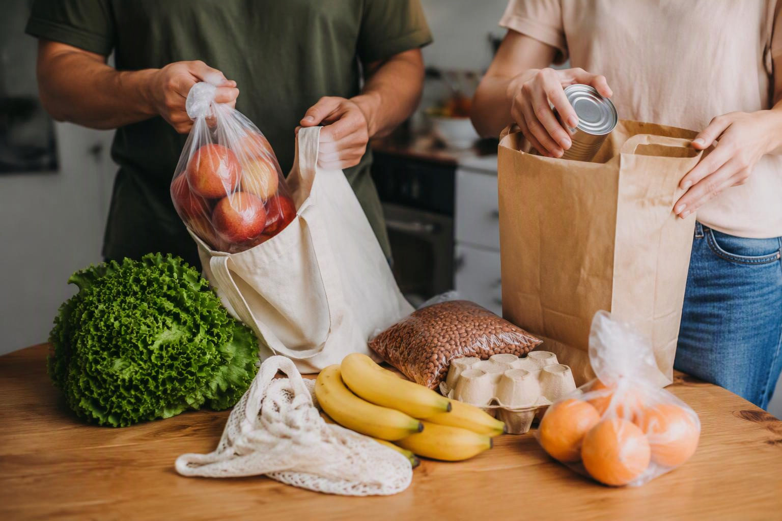 Duas pessoas dividem a tarefa de guardar compras sobre uma mesa de cozinha.