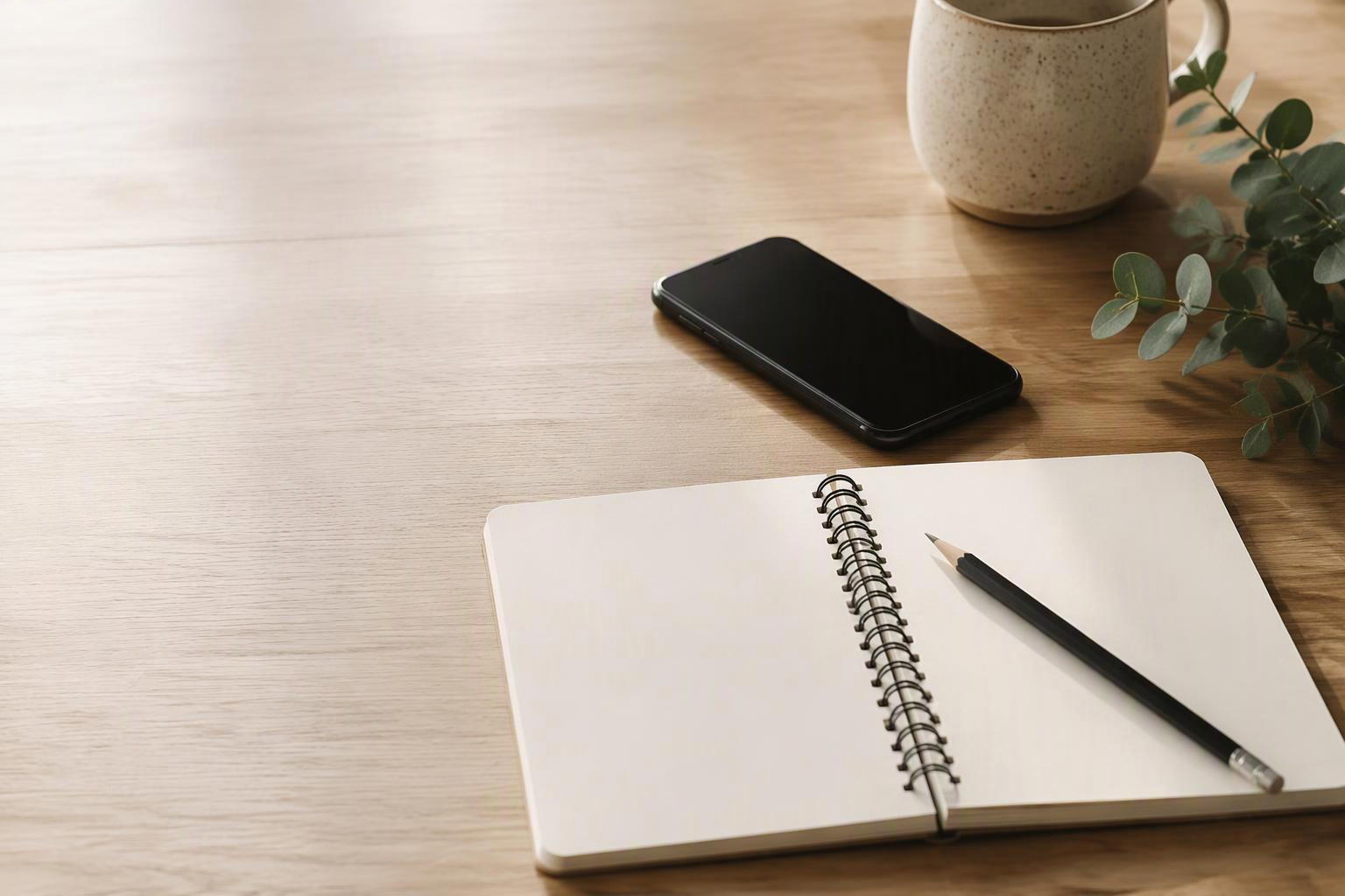 Celular com tela apagada ao lado de caderno e lápis sobre uma mesa.